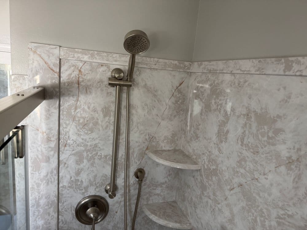 Modern shower interior featuring marble walls and a sleek handheld showerhead.