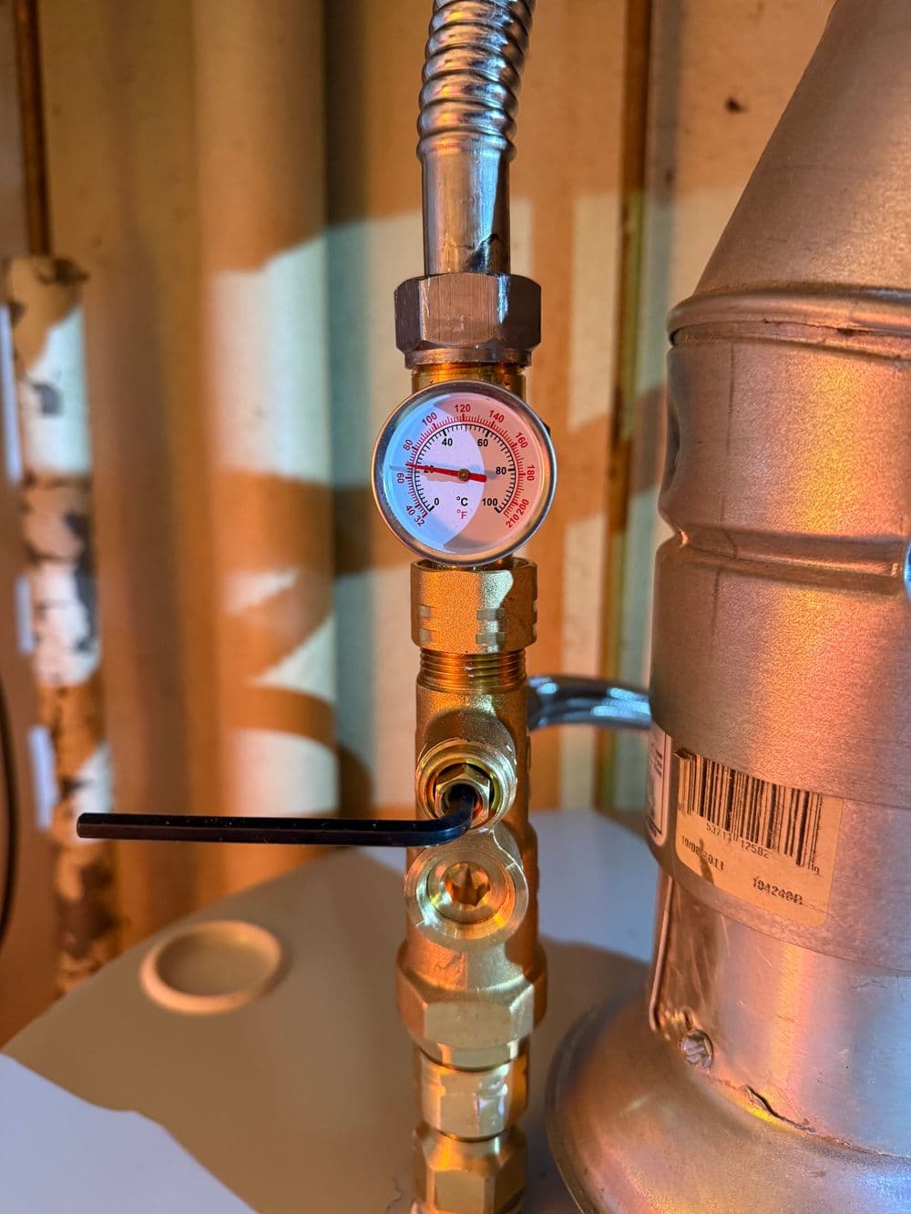Pressure gauge on a brass valve connected to a water heater for monitoring temperature.