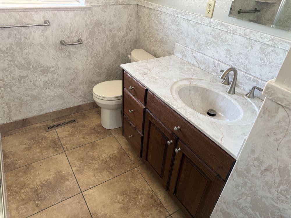 Modern bathroom with toilet, sink, and marble-patterned walls and tiled floor.