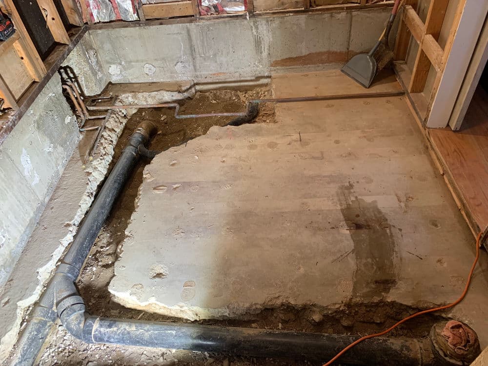 Renovation project showing exposed basement floor with plumbing pipes and construction tools.