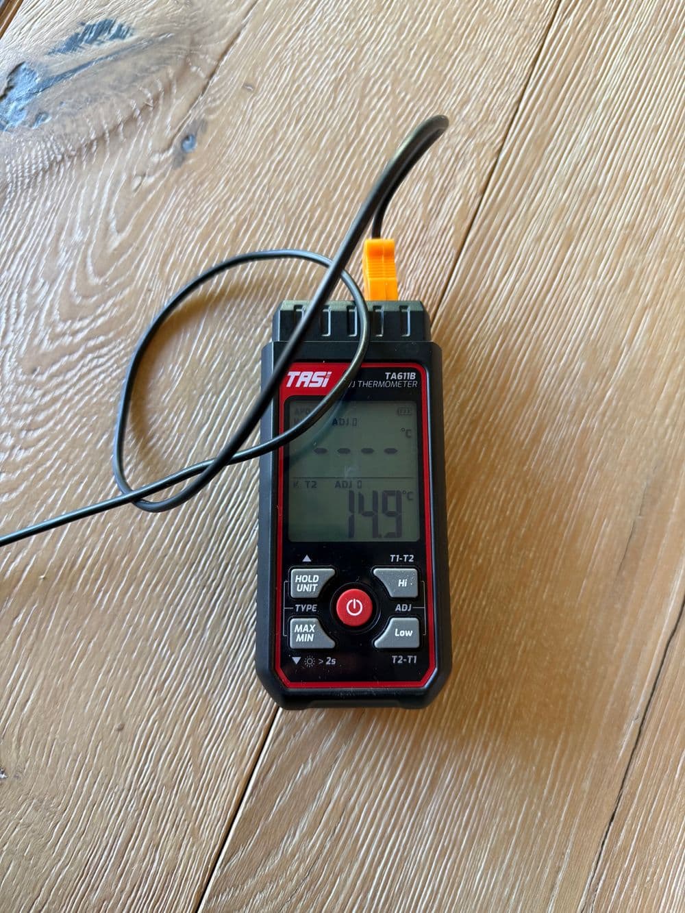 Digital thermometer displaying 149°F on wooden surface with probe cable attached.
