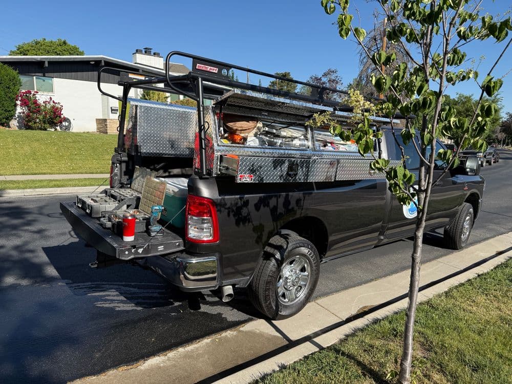 Black pickup truck with a utility rack, tools, and equipment in the bed parked on a residential street.